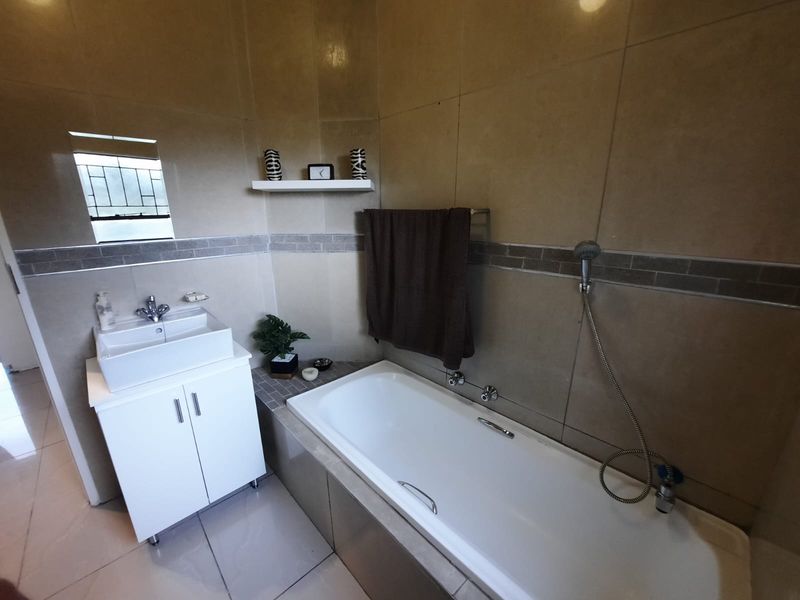 A functional bathroom featuring a white vanity with a vessel sink, a bathtub with a handheld shower mixer, and neutral-toned wall and floor tiling.