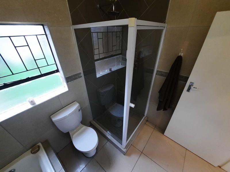 A functional bathroom featuring a tiled shower enclosure, a standard toilet, and tiled flooring with natural light from a window.