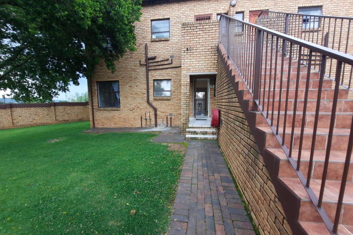 Exterior view of a brick apartment building featuring an external staircase, paved walkway, and communal garden area.
