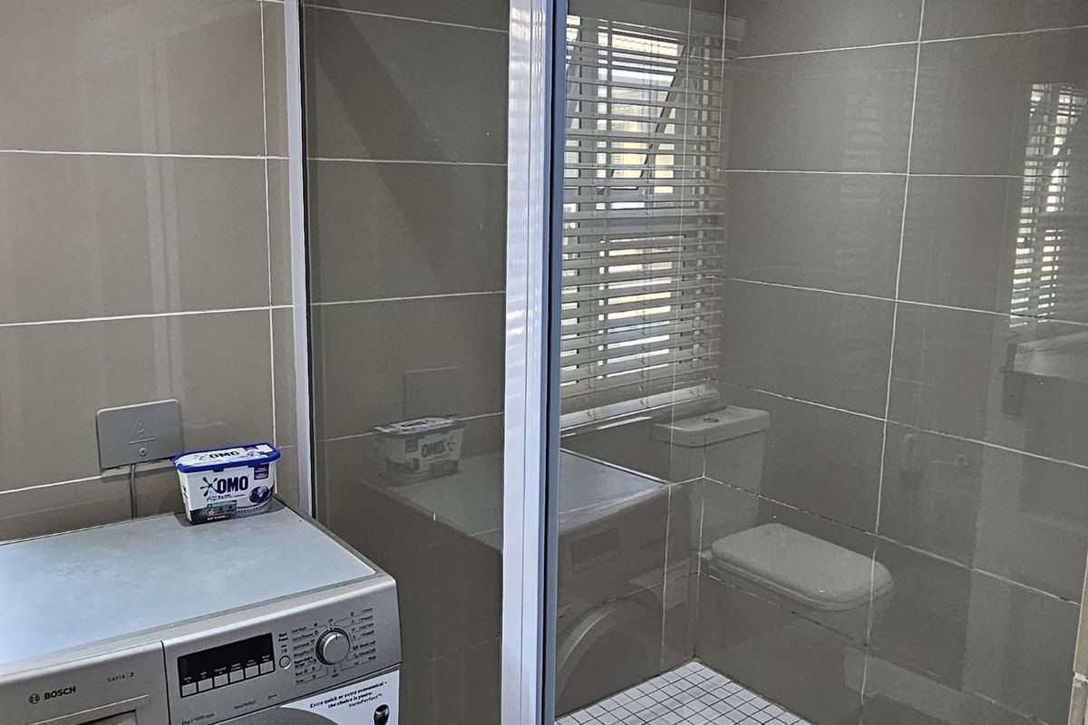 A modern bathroom featuring a walk-in shower with glass enclosure, tiled walls, and a dedicated space for a washing machine.