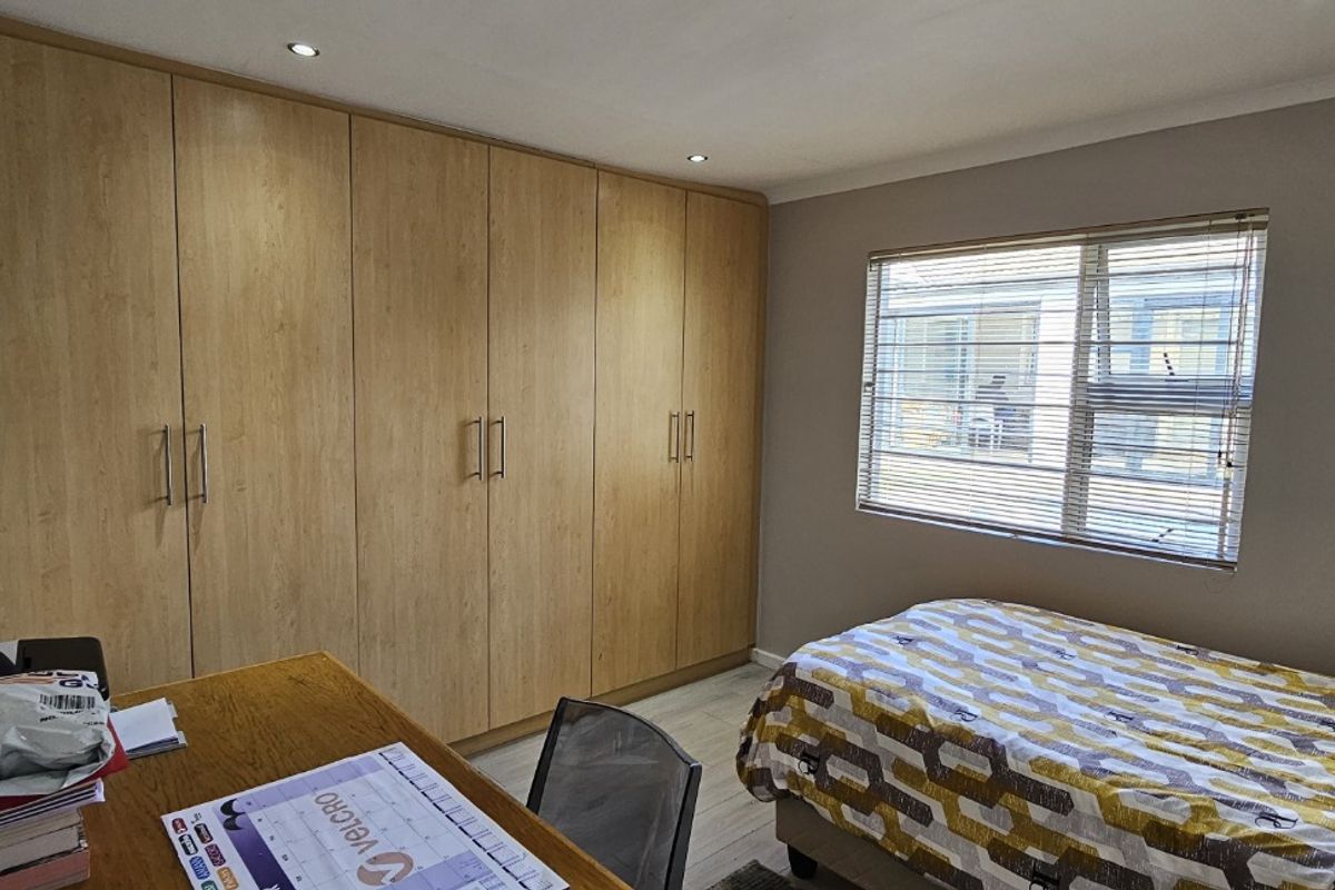 A well-maintained bedroom featuring extensive built-in wooden cabinetry, recessed ceiling lighting, and a window with fitted blinds.