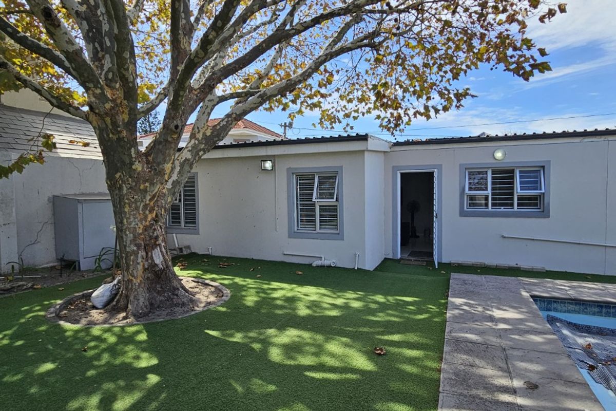 Rear exterior view of the flat featuring a small swimming pool, artificial lawn, mature tree, and direct access to the living area.
