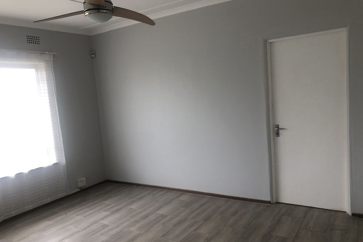 A clean, empty bedroom featuring modern laminate flooring, a ceiling fan, and neutral grey walls, offering a blank canvas for personalization.