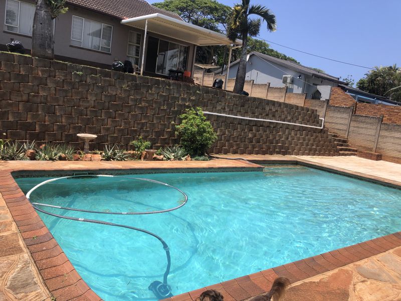 Outdoor pool area featuring a swimming pool, paved surround, and a tiered retaining wall leading up to a covered patio.