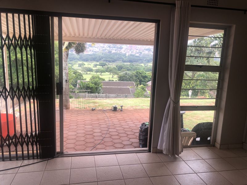 A view from an interior space looking out onto a covered patio with tiled flooring and a scenic garden outlook.
