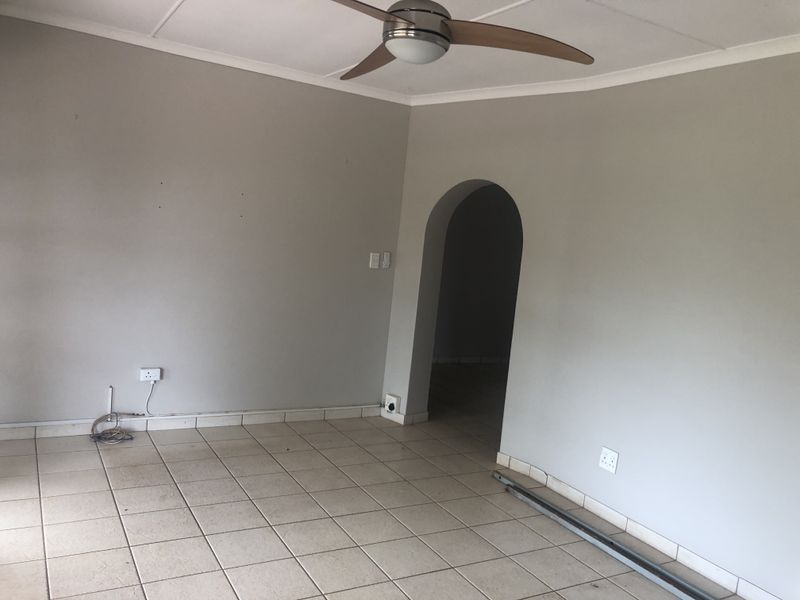An empty living room featuring tiled flooring, a ceiling fan, and a distinctive arched doorway leading to an adjacent space.