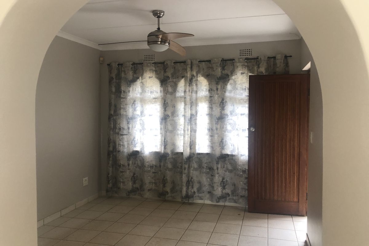 An empty living room featuring tiled flooring, a ceiling fan, and a distinctive arched entryway leading into the space.