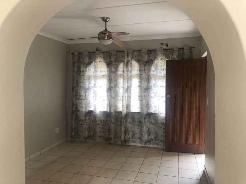 An empty living room featuring tiled flooring, a ceiling fan, and a distinctive arched entryway leading into the space.