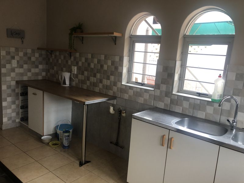 A functional scullery area featuring a stainless steel sink, tiled splashback, built-in cabinetry, and arched windows with security bars.