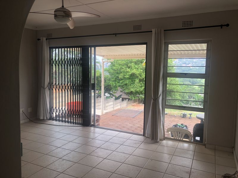 Spacious living area featuring neutral tiled flooring, a ceiling fan, and large sliding doors providing direct access to the outdoor patio and garden.