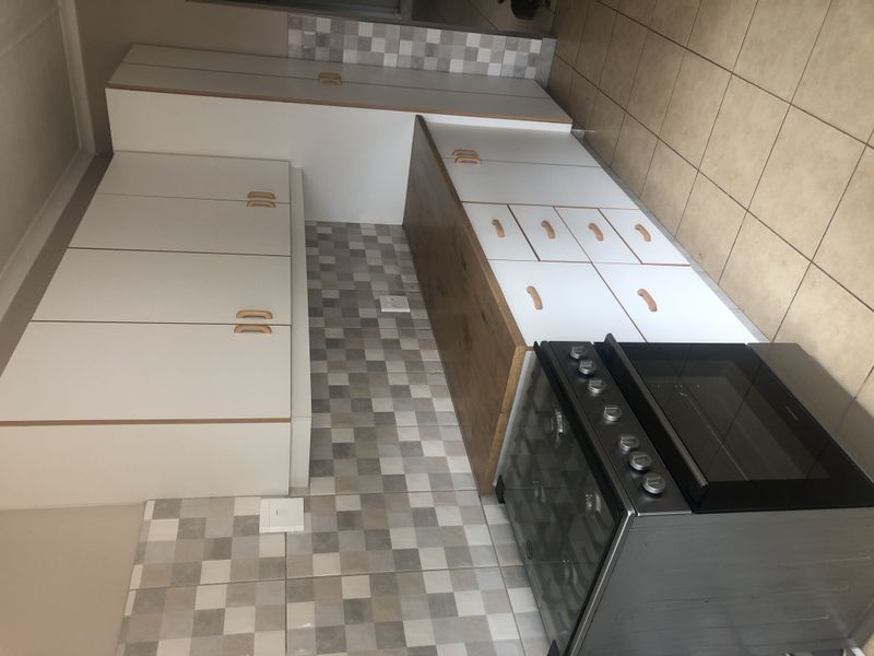 A clean, functional kitchen featuring white cabinetry, a wood-look countertop, a gas stove with oven, and a modern mosaic-style tiled backsplash.