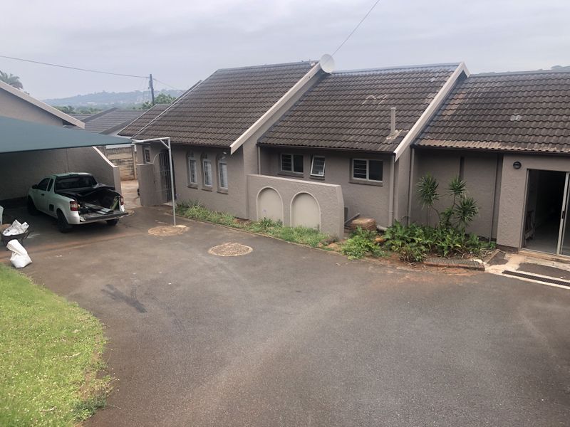 Front exterior view of a residential property featuring a tiled roof, paved driveway, and an attached carport area.