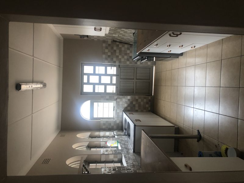 A functional kitchen featuring tiled flooring, built-in cabinetry, a tiled backsplash, and arched windows providing natural light.