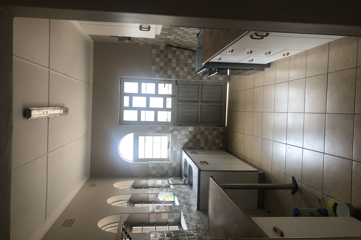 A functional kitchen featuring tiled flooring, built-in cabinetry, a tiled backsplash, and arched windows providing natural light.