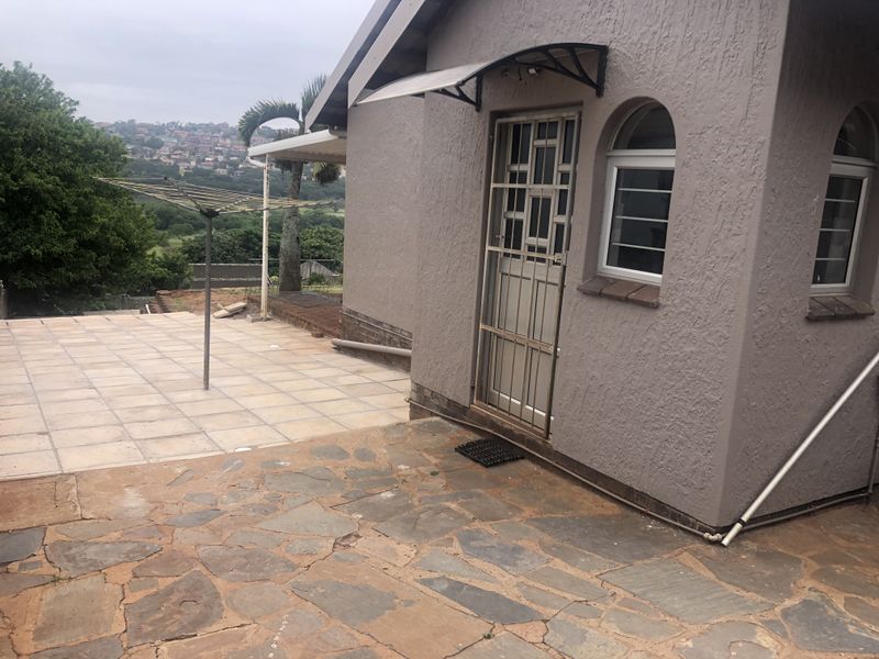 Rear exterior view featuring a tiled patio, stone paving, security gate, and arched windows with a textured wall finish.