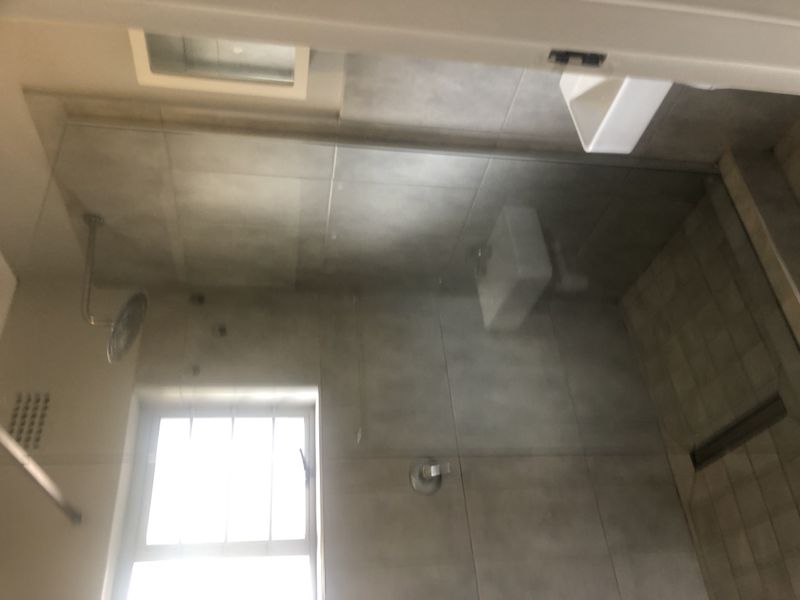 A modern bathroom featuring a walk-in shower with a glass screen, rain shower head, and wall-mounted basin with neutral tiling.