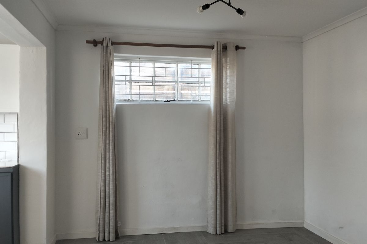A view of a living area with tiled flooring, featuring a small window with security bars and a glimpse into the adjacent kitchen area.