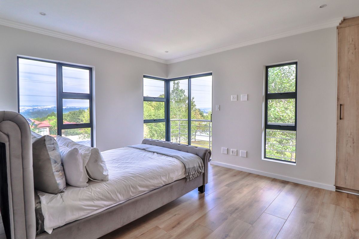 Modern bedroom featuring laminate flooring, built-in wardrobes, and large aluminium windows providing natural light and access to a balcony.