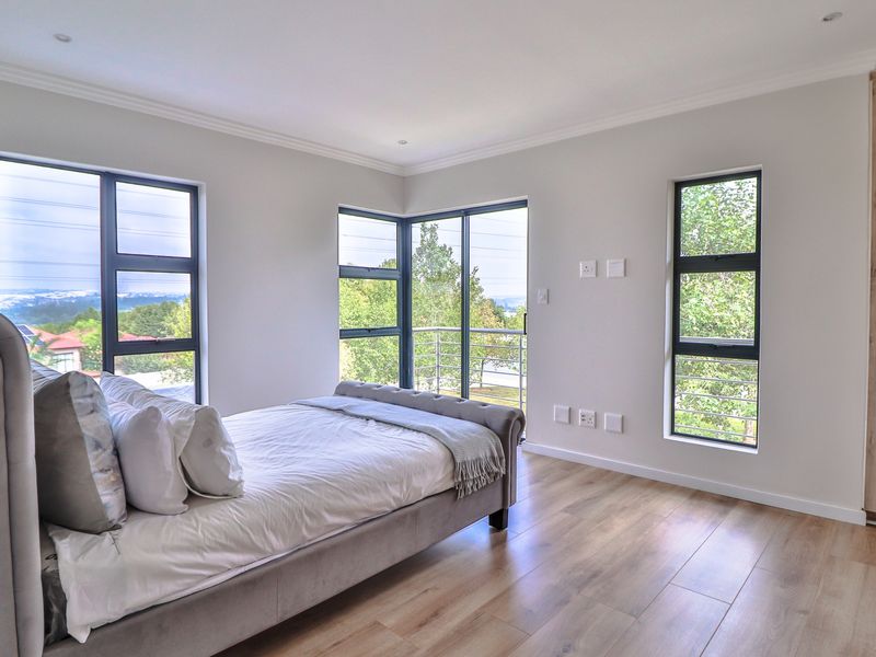 Modern bedroom featuring laminate flooring, built-in wardrobes, and large aluminium windows providing natural light and access to a balcony.