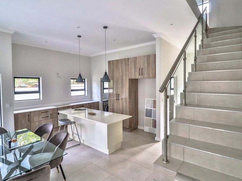 Modern open-plan kitchen and dining area featuring sleek cabinetry, a central island, and a contemporary staircase with a glass balustrade.