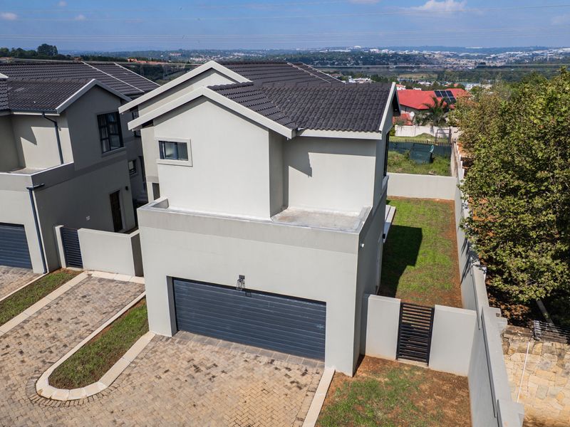 Aerial view of a modern residential property featuring a tiled roof, paved driveway, integrated garage, and enclosed garden area.