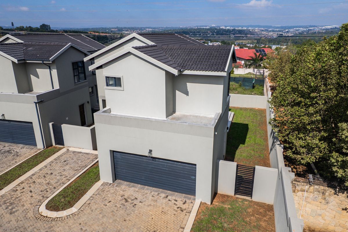 Aerial view of a modern residential property featuring a tiled roof, paved driveway, integrated garage, and enclosed garden area.