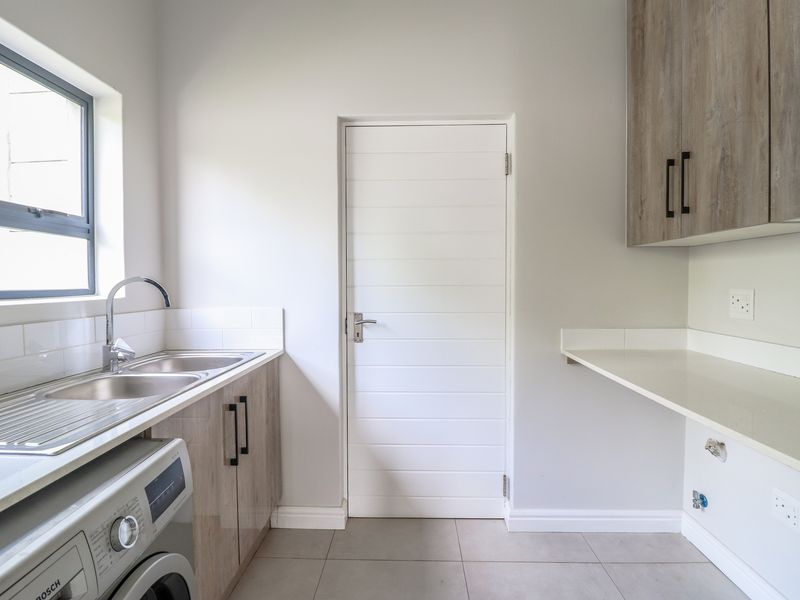 A clean and modern laundry room featuring built-in cabinetry, stone countertops, a stainless steel sink, and dedicated plumbing connections for appliances.