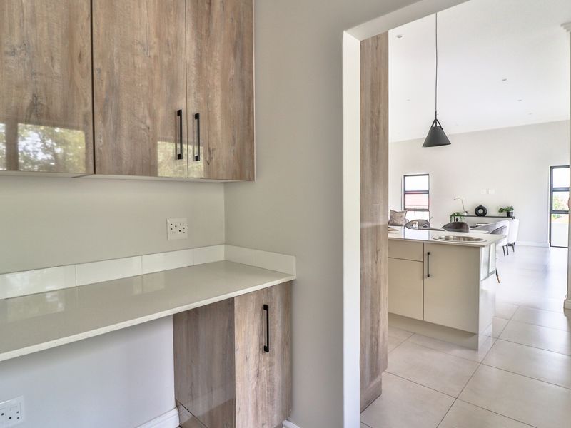 A clean, modern scullery area featuring wood-finish cabinetry, stone countertops, and a tiled backsplash, with a seamless transition into the open-plan living space.