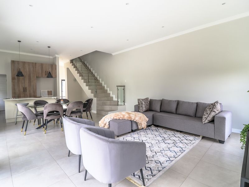 Spacious open-plan living and dining area featuring modern tiled floors, a sleek staircase with glass balustrade, and a contemporary kitchen with integrated cabinetry.