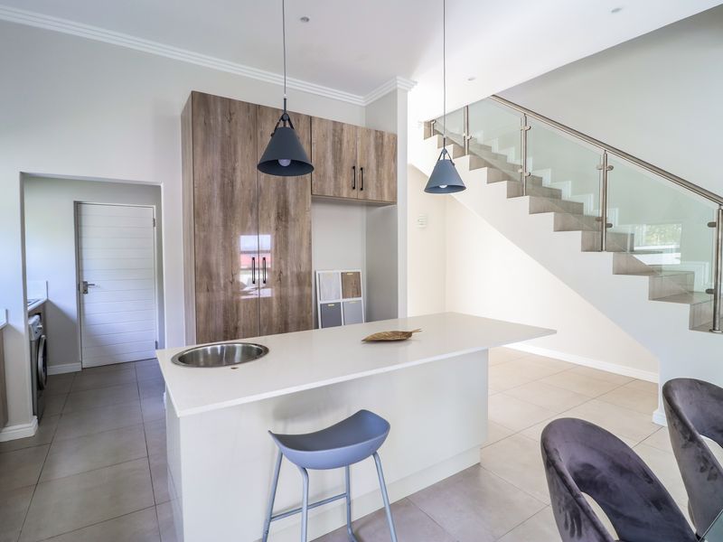 Modern kitchen featuring a central island with a sink, wood-finish cabinetry, and an adjacent staircase with a contemporary glass balustrade.