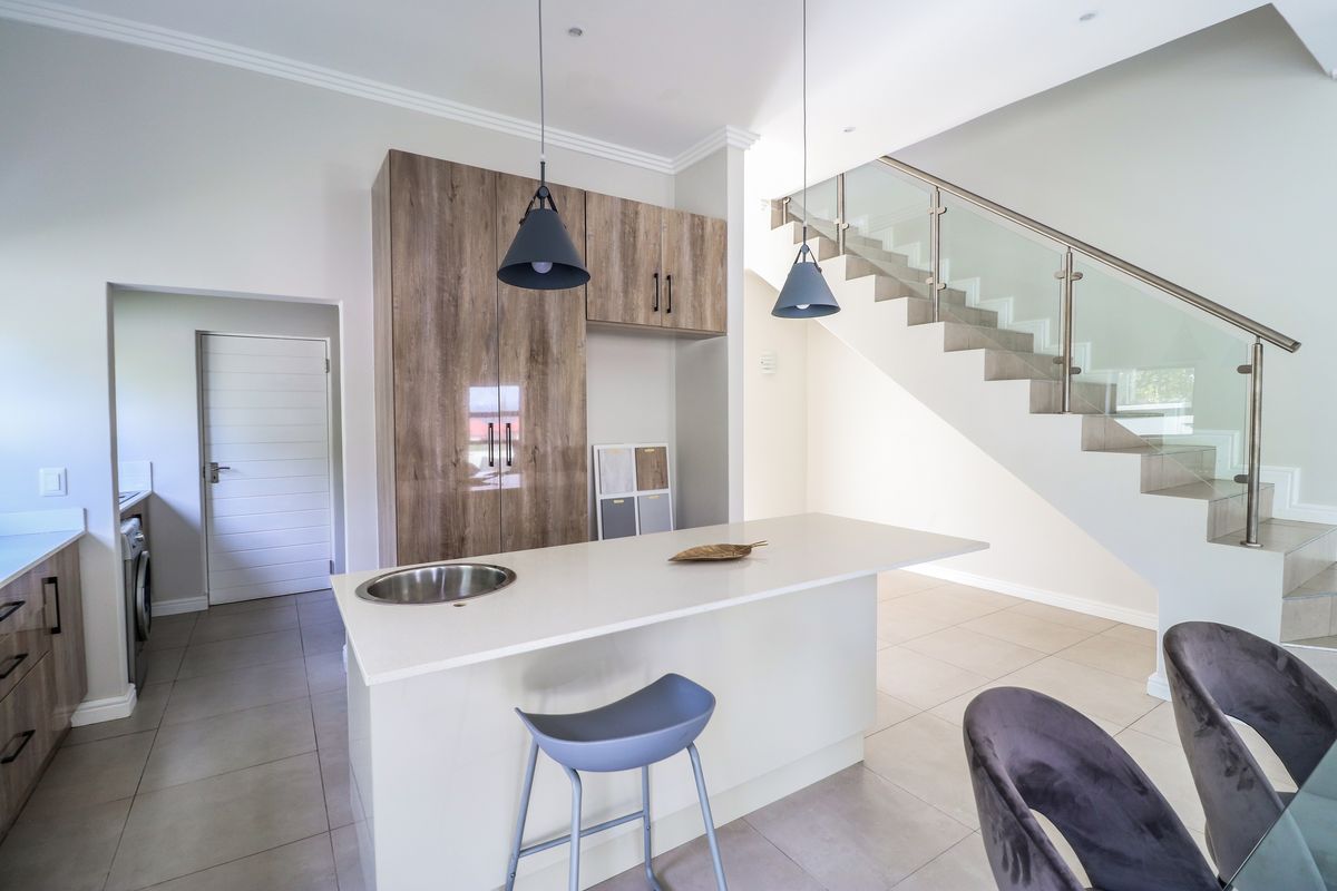 Modern kitchen featuring a central island with a sink, wood-finish cabinetry, and an adjacent staircase with a contemporary glass balustrade.