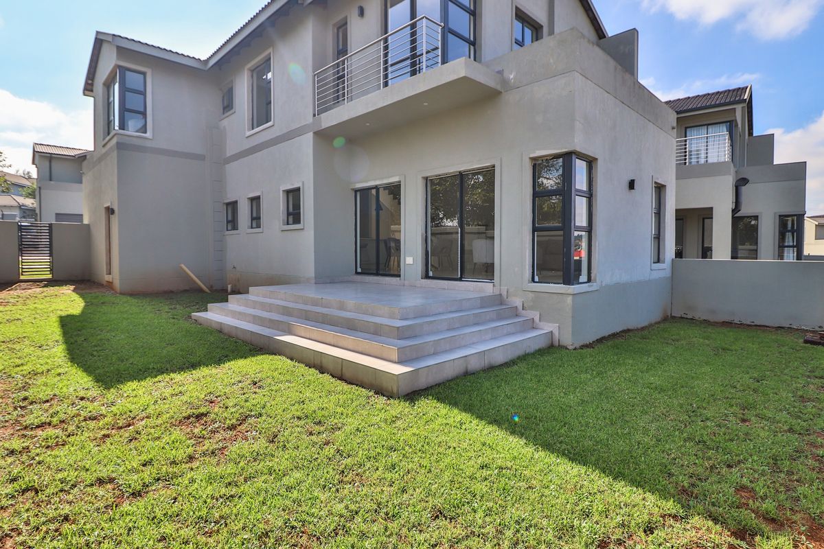 Rear view of a modern two-story house featuring a tiled patio, a balcony with metal railings, and a well-maintained lawn.