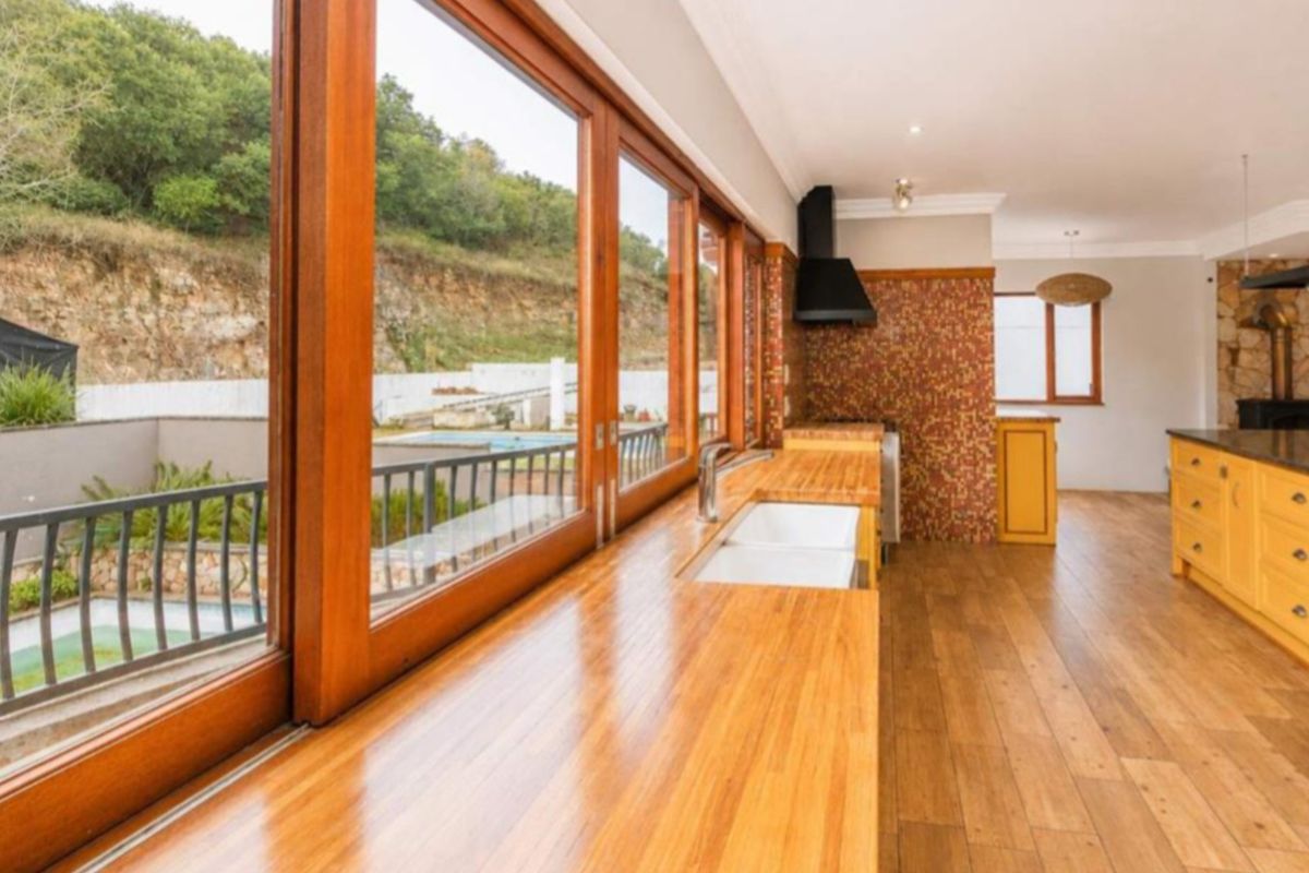 Spacious kitchen featuring warm timber cabinetry, wooden countertops, a double basin sink, and large windows offering scenic views of the outdoor pool area.
