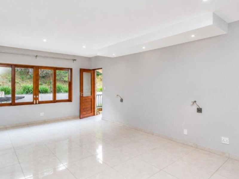 A bright, empty living room featuring neutral tiled flooring, recessed ceiling lighting, and timber-framed windows and doors.