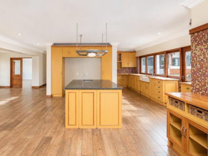 Spacious open-plan kitchen featuring light wood cabinetry, a central island with granite countertops, a farmhouse sink, and warm-toned mosaic tile accents.
