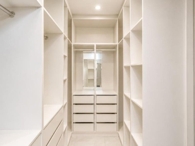 A modern, well-organized walk-in closet featuring extensive built-in shelving, drawers, and hanging space with clean, minimalist finishes.