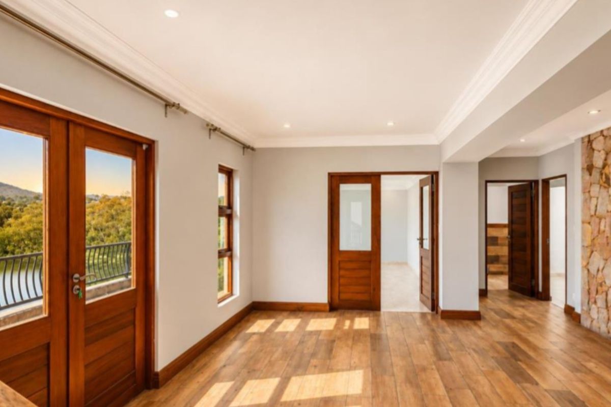Spacious living area featuring timber flooring, a natural stone feature wall, and direct access to a balcony with scenic views.