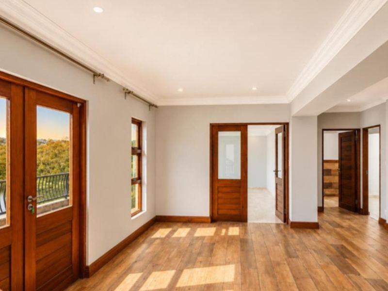 Spacious living area featuring timber flooring, a natural stone feature wall, and direct access to a balcony with scenic views.