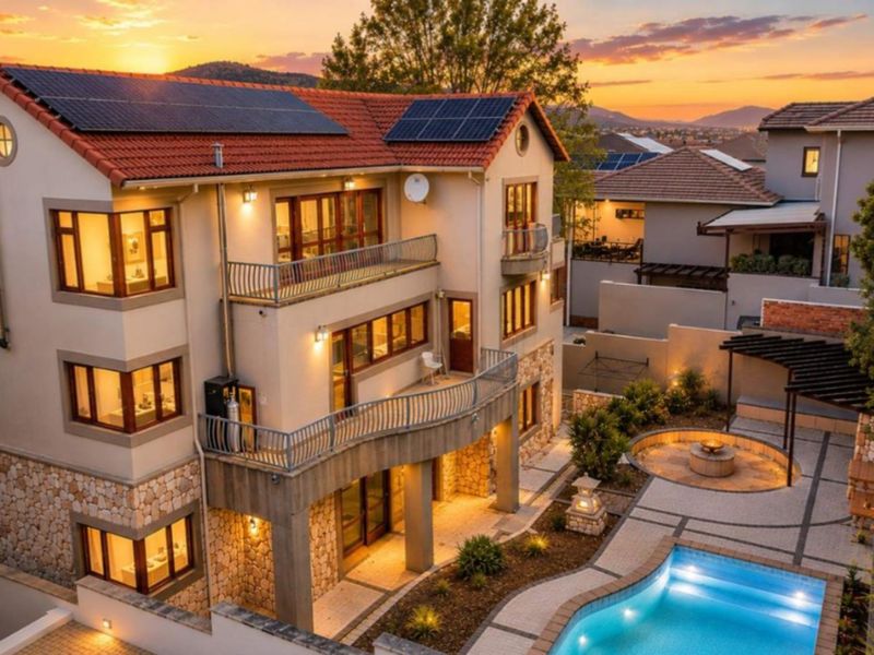 A multi-story residence featuring stone cladding, multiple balconies, solar panels, and a landscaped rear garden with a swimming pool and fire pit area.