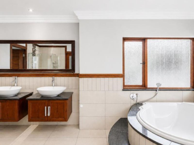 A well-maintained bathroom featuring a double vanity with vessel sinks, granite countertops, wooden cabinetry, and a built-in corner bathtub with tiled surround.
