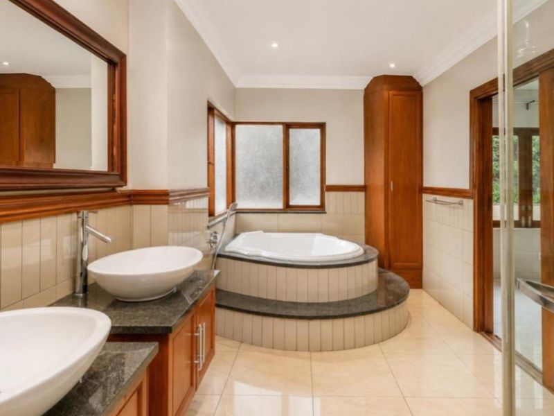 Spacious bathroom featuring a double vanity with granite countertops, built-in cabinetry, a sunken bathtub, and a separate glass-enclosed shower.