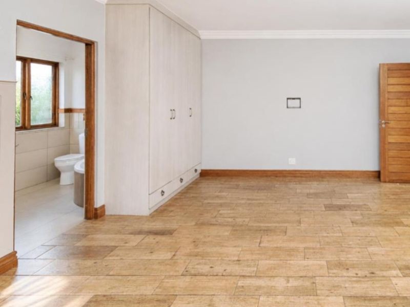 Spacious bedroom featuring light-toned built-in cupboards, wood-look tiled flooring, and direct access to an en-suite bathroom.