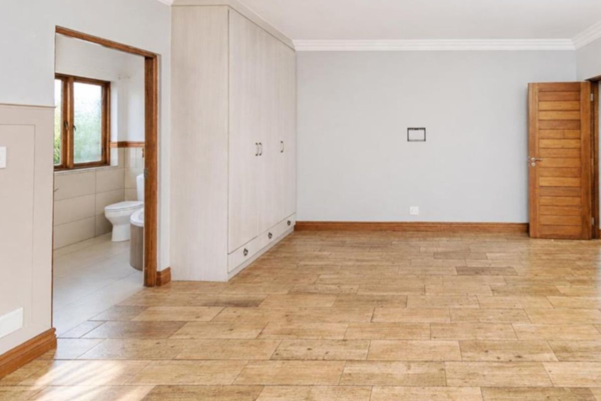 Spacious bedroom featuring light-toned built-in cupboards, wood-look tiled flooring, and direct access to an en-suite bathroom.