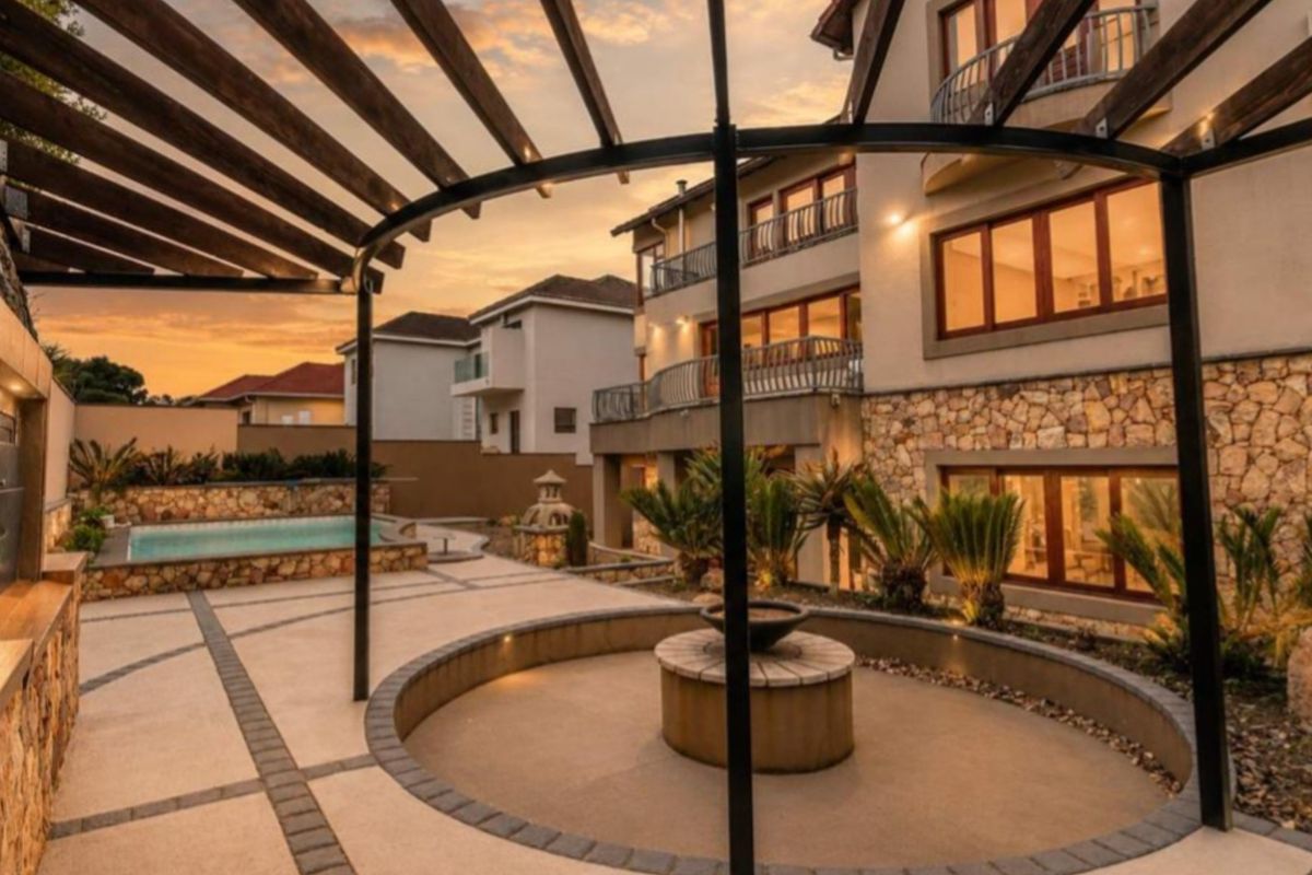 Spacious rear exterior featuring a paved patio, pergola, swimming pool, and stone-clad building facade with balconies, perfect for outdoor entertaining.