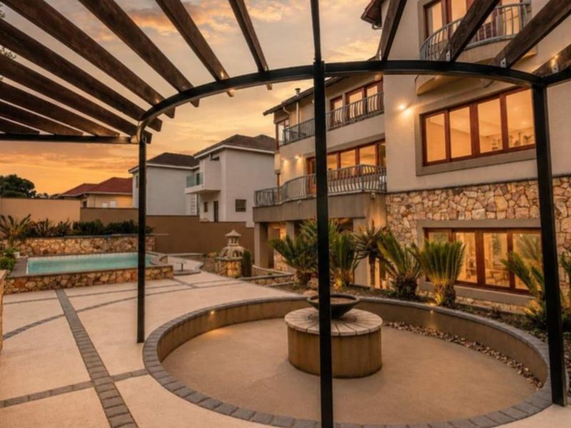 Spacious rear exterior featuring a paved patio, pergola, swimming pool, and stone-clad building facade with balconies, perfect for outdoor entertaining.