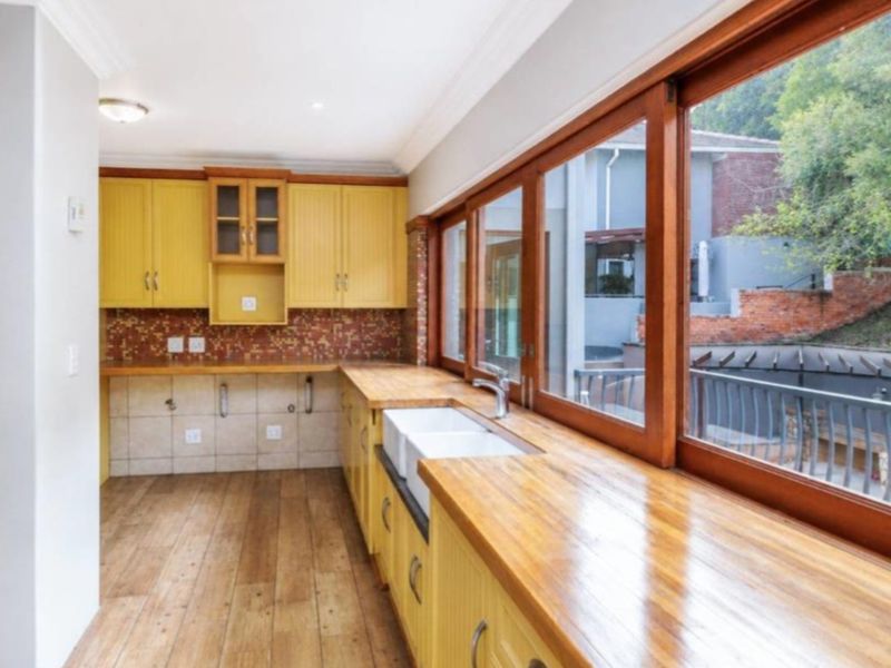 A bright kitchen featuring yellow cabinetry, wooden countertops, a double farmhouse sink, and large timber-framed windows overlooking the rear garden area.