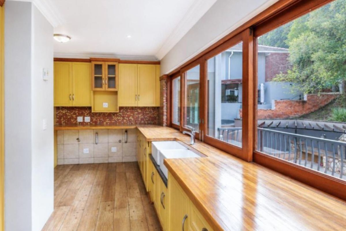 A bright kitchen featuring yellow cabinetry, wooden countertops, a double farmhouse sink, and large timber-framed windows overlooking the rear garden area.