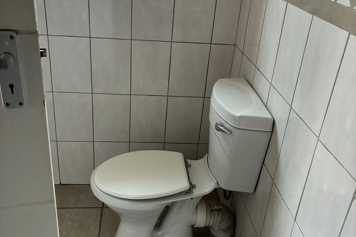 A compact bathroom featuring tiled walls and floors, a standard toilet, and a pedestal basin, with a window providing natural light.