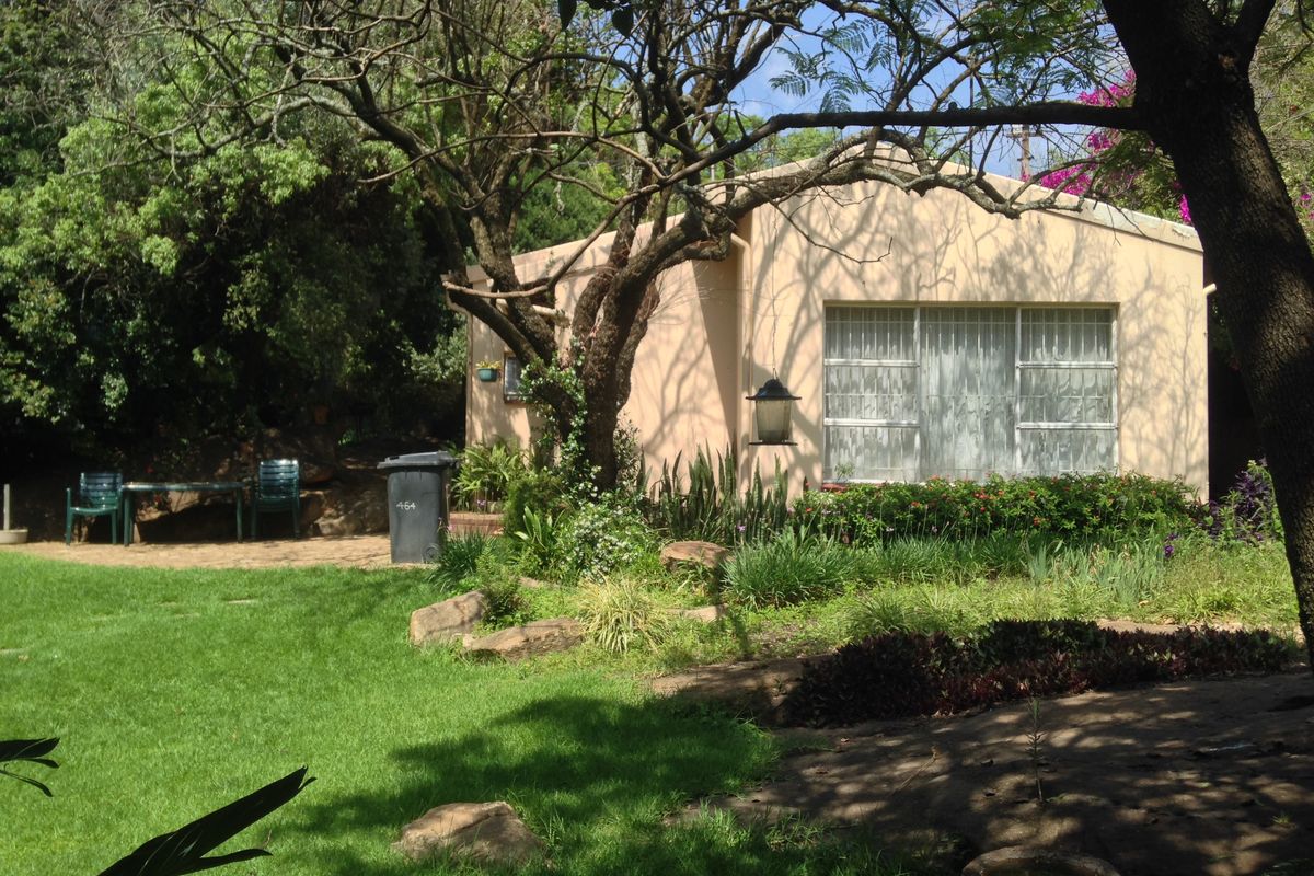 A view of the rear exterior of the house featuring a paved patio area, established garden, and mature trees.