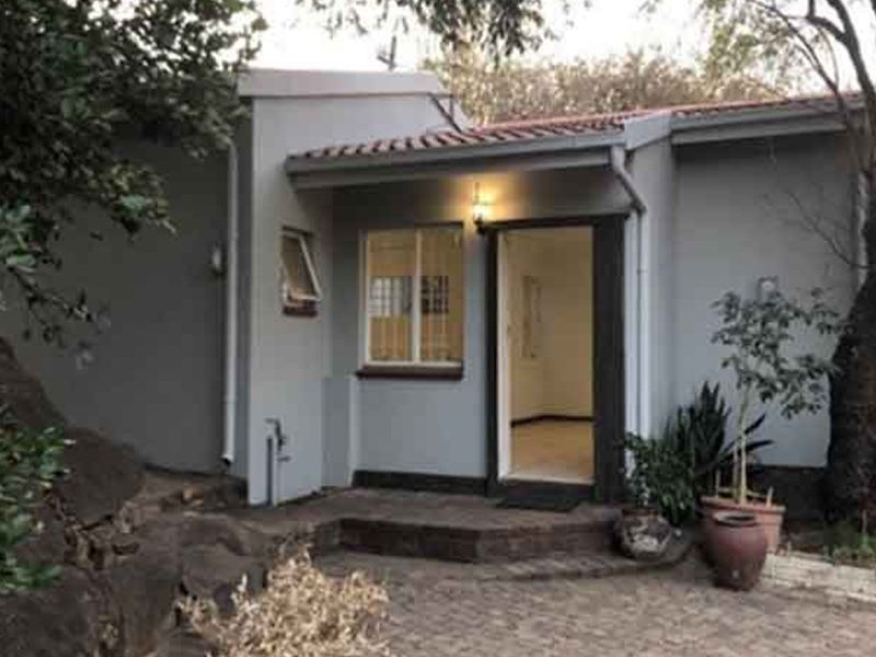 A view of the front entrance featuring a paved patio area, tiled roof, and exterior lighting, set against a natural garden backdrop.